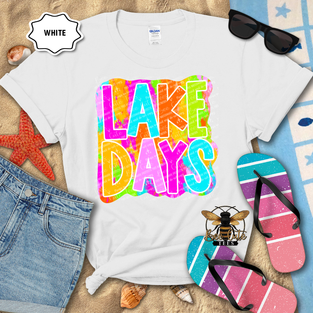 White t-shirt with 'Lake Days' design, sunglasses, and flip-flops on a beach-themed background.