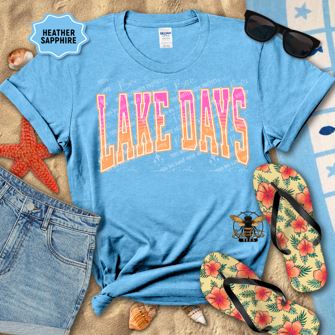 Blue t-shirt with 'Lake Days' print on a sandy surface with beach accessories.
