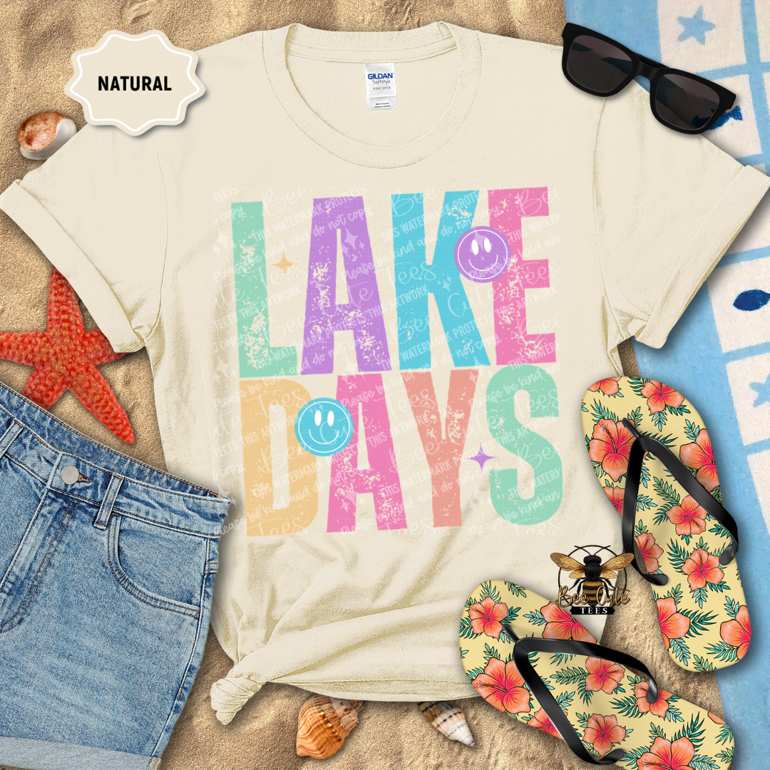 Beige t-shirt with 'Lake Days' design on a beach-themed background with sunglasses, flip-flops, and starfish.