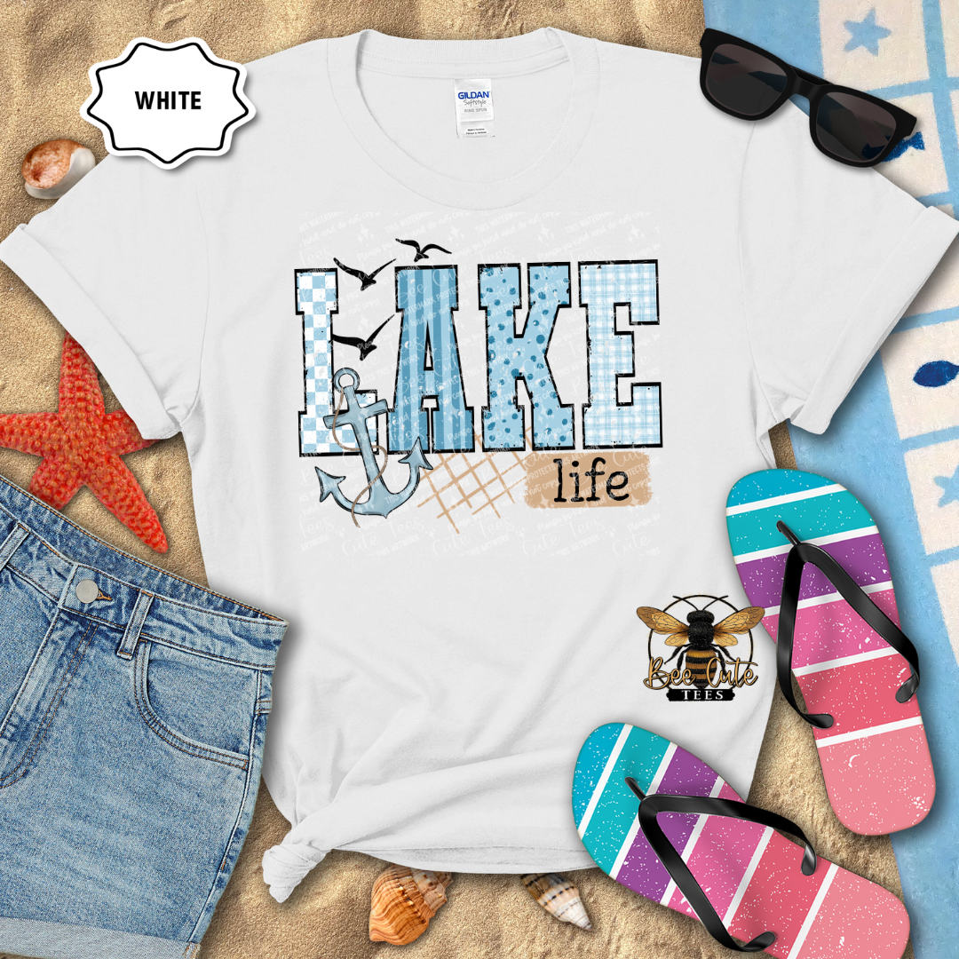White t-shirt with 'Lake life' design on a beach-themed background with sunglasses, flip-flops, and denim shorts.