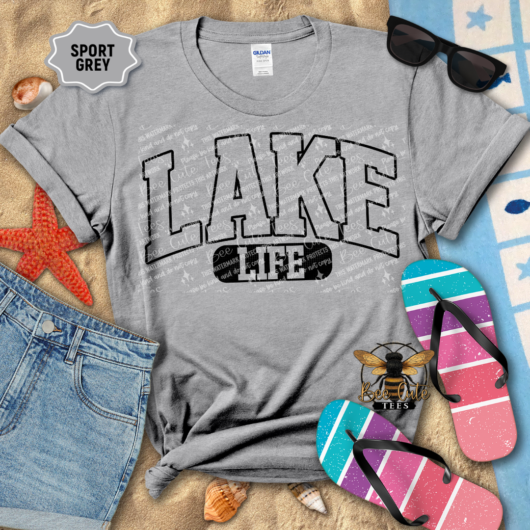 Gray t-shirt with 'Lake Life' design on a beach-themed background with flip-flops and sunglasses.