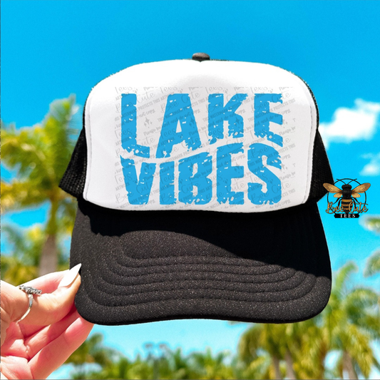 Trucker hat with 'Lake Vibes' text held by a hand against a blue sky background