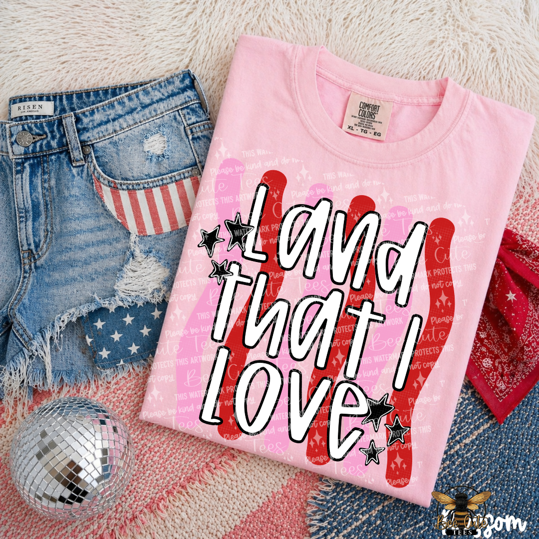 Pink t-shirt with 'Land That I Love' text on a textured surface with denim and disco ball.
