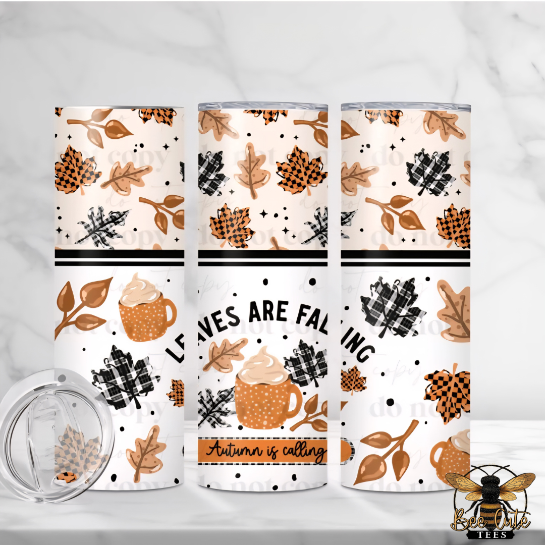 Three insulated tumbler cups with autumn-themed fall leaves, pinecones, plaid patterns, and a mug graphic are displayed on a white marble surface. One cup is shown with its clear lid removed in the foreground.