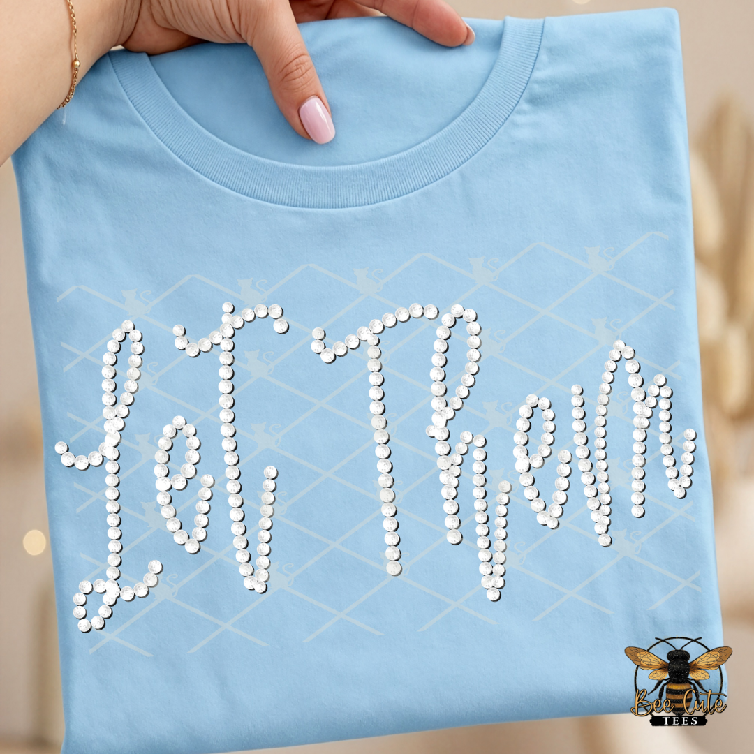 Light blue t-shirt with 'Let Them' text made of faux white pearls, held by a hand.
