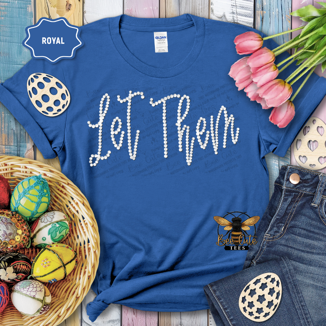 Blue t-shirt with 'Let Them' text, surrounded by Easter decorations on a wooden surface.