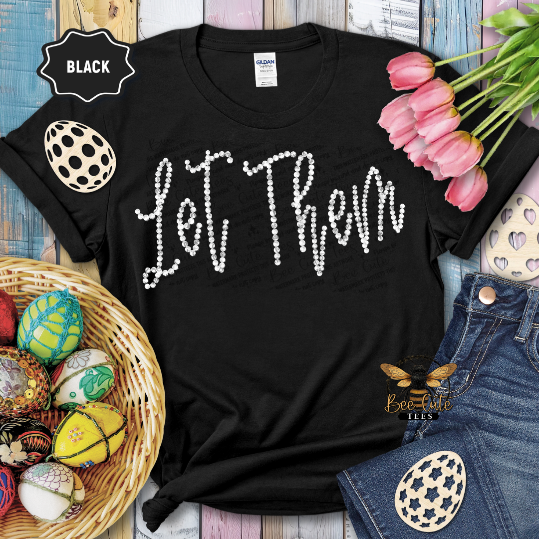 Black t-shirt with 'Let Them' text, Easter decorations, and jeans on a wooden surface.