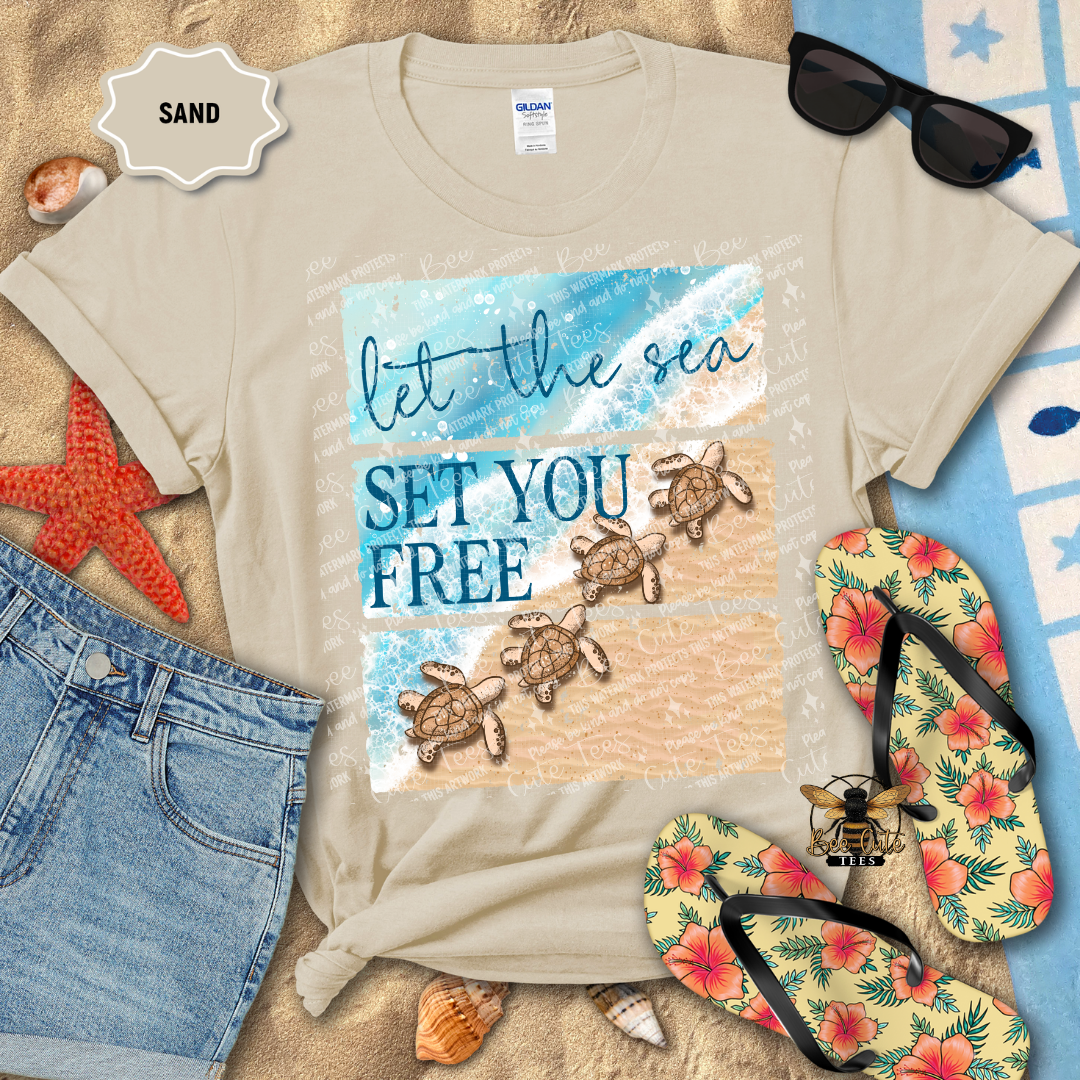 Beige t-shirt with sea turtle design and text 'let the sea set you free' on a sandy background with flip-flops and sunglasses.