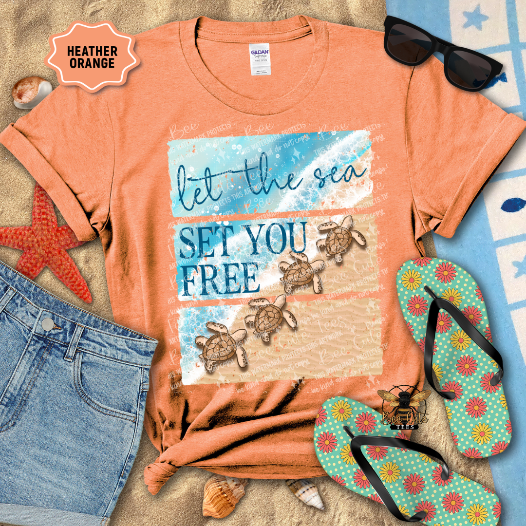 Orange t-shirt with turtle design and text 'let the sea SET YOU FREE' on a beach-themed background with sunglasses, flip-flops, and starfish.