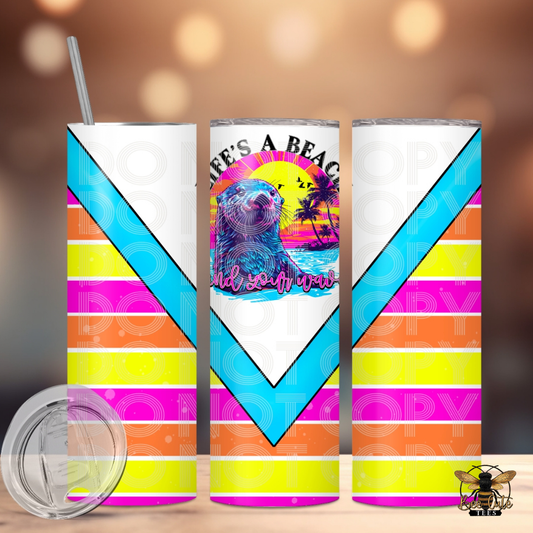 Bright and colorful 20 oz tumbler featuring a neon-style beach sunset with an otter illustration and “Life’s a Beach, Find Your Wave” wording, accented with bold pink, orange, yellow, and turquoise stripe details, displayed with a lid and metal straw against a softly lit background.

