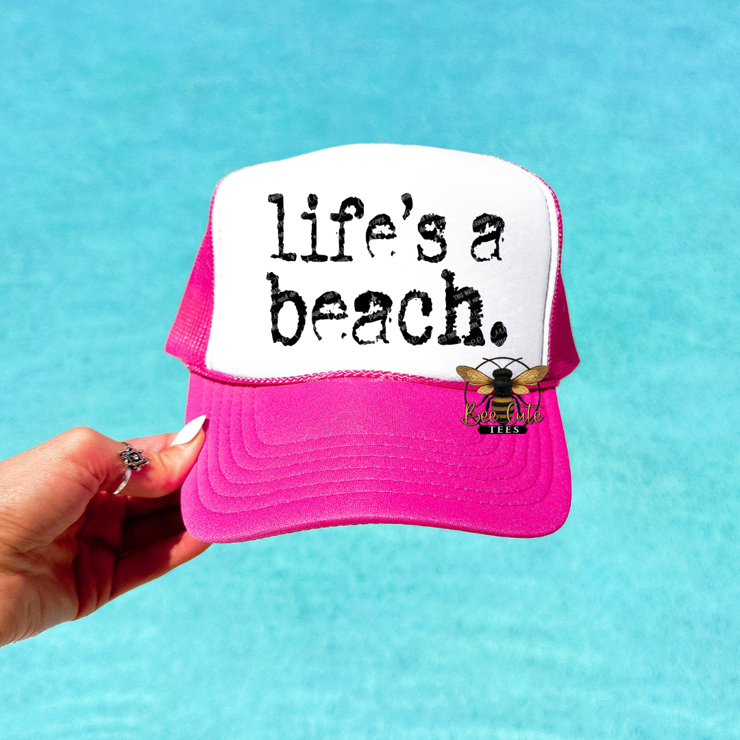 Pink and white cap with 'life's a beach' text and bee logo against a blue background