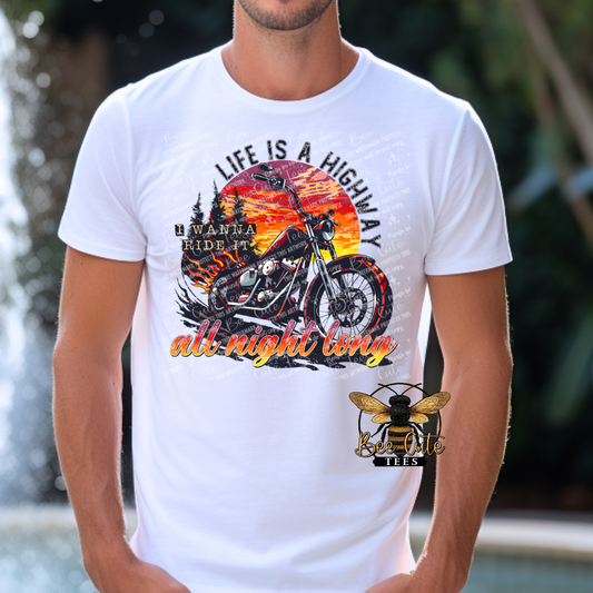 Man wearing a white graphic tee featuring a black motorcycle in front of a colorful sunset with the phrase “Life Is a Highway” in bold vintage-inspired lettering.
