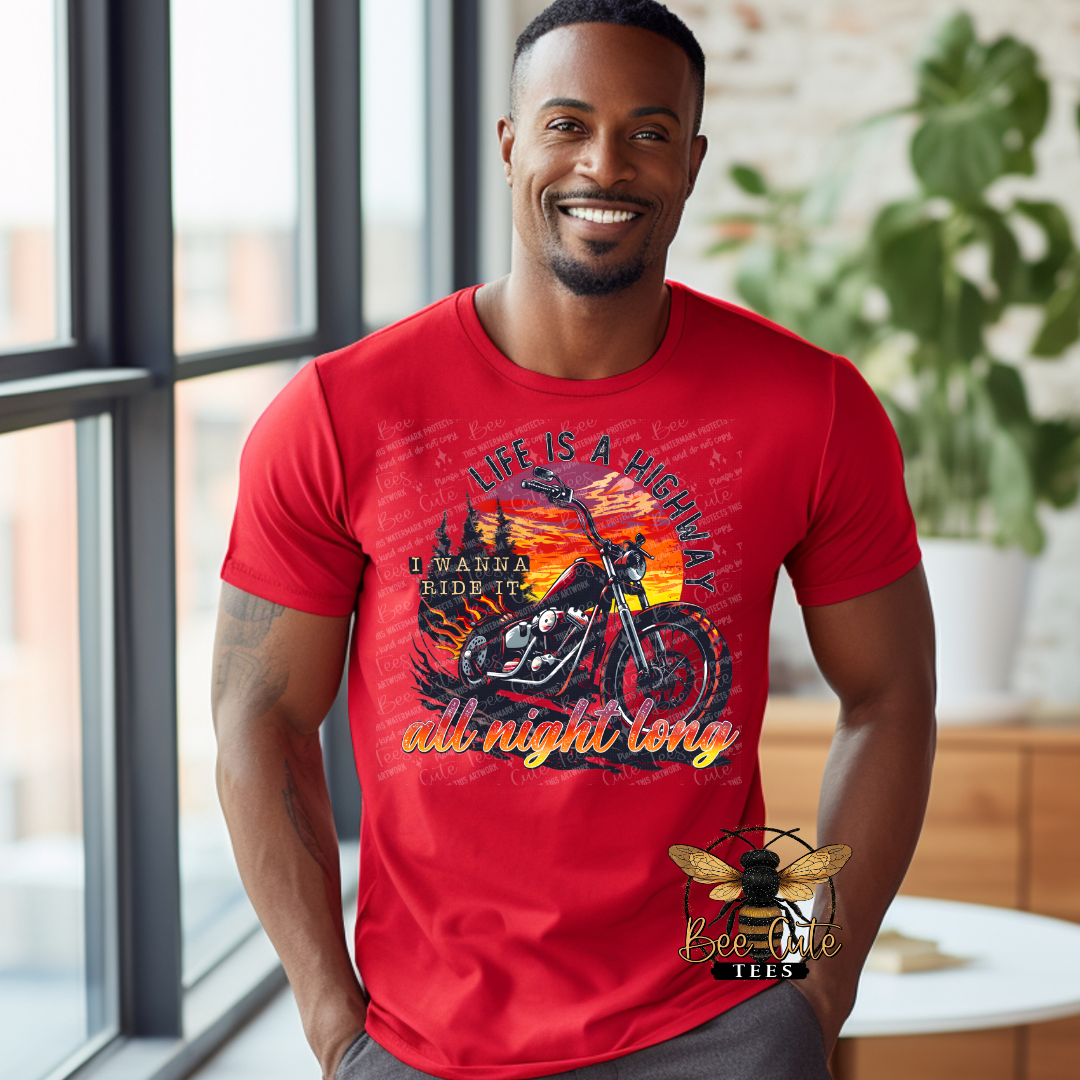 Smiling man wearing a bright red graphic tee featuring a motorcycle in front of a sunset scene with the phrase “Life Is a Highway” in bold retro-style lettering.
