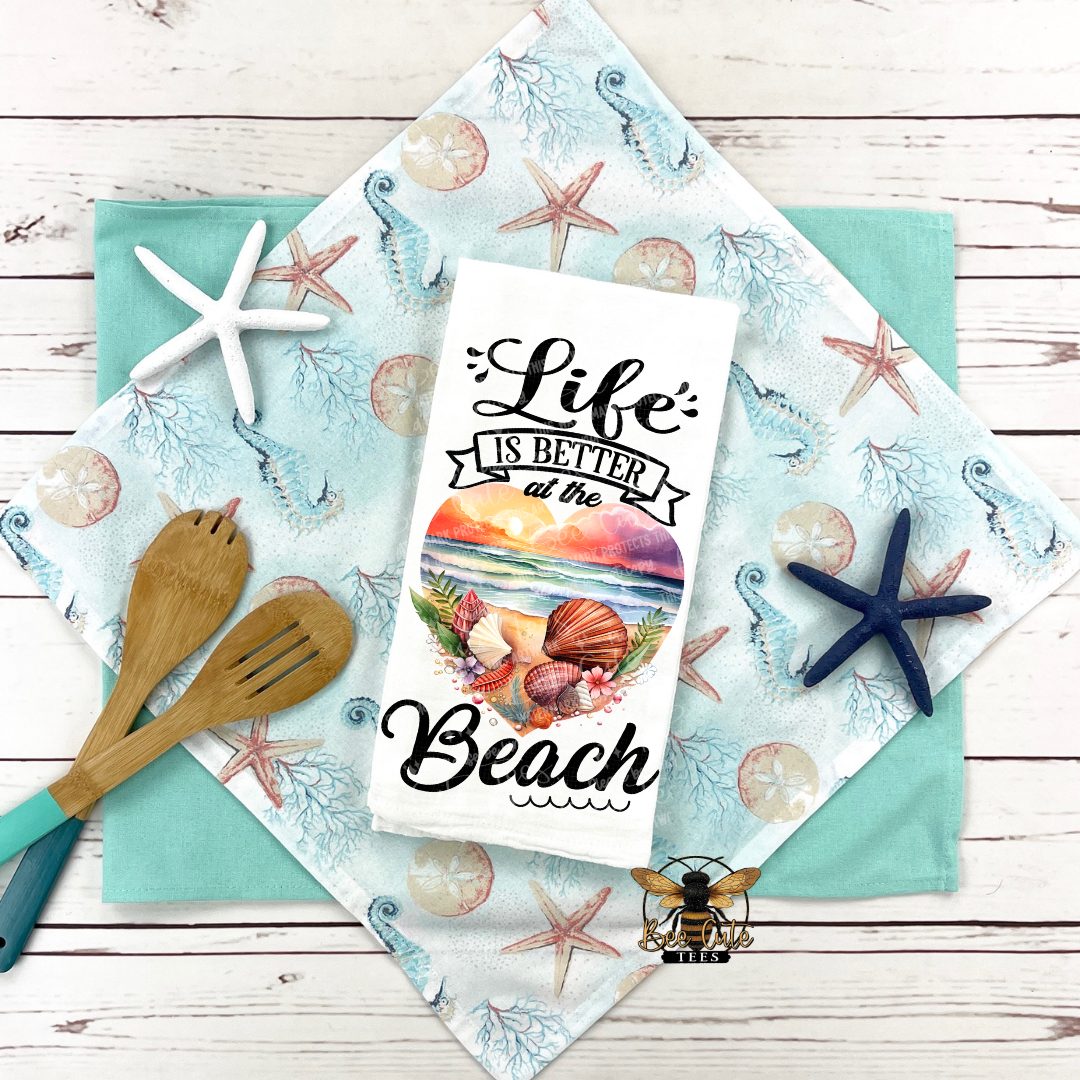 Beach-themed towel with 'Life is Better at the Beach' text on a wooden surface with starfish and seashells.