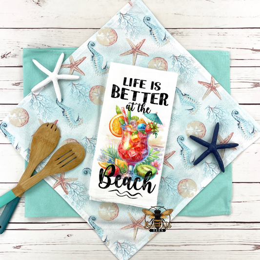 Beach-themed towel with a cocktail graphic and 'Life is Better at the Beach' text on a wooden surface.