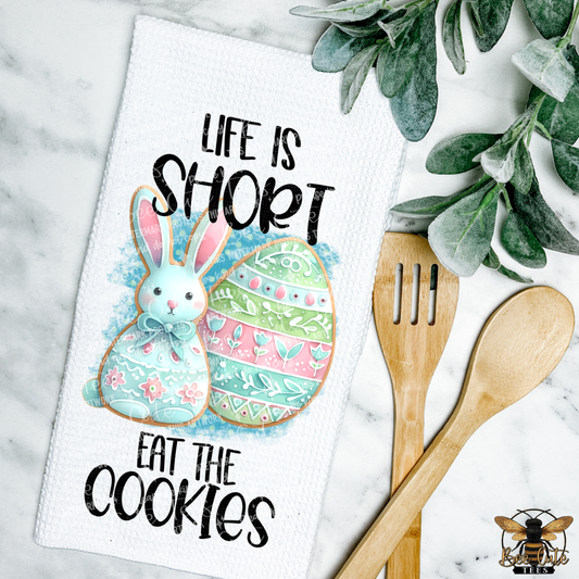Easter-themed towel with a cookie design, wooden utensils, and greenery on a marble background.