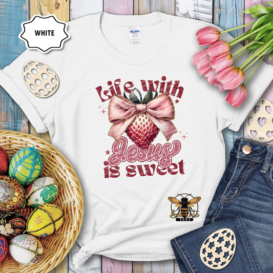 White t-shirt with 'Life with Jesus is sweet' design on a wooden surface with Easter decorations.