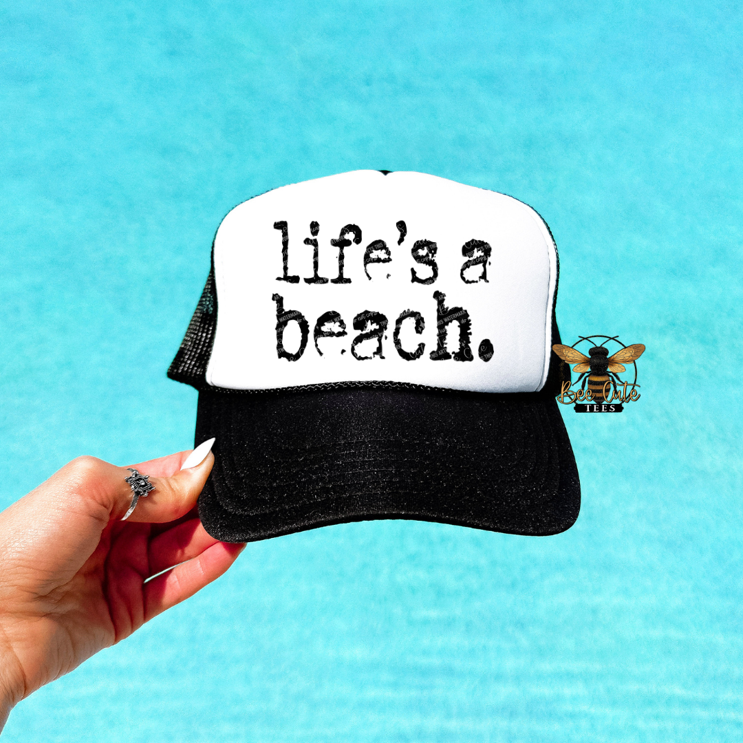 Trucker hat with 'life's a beach.' text held against a blue background