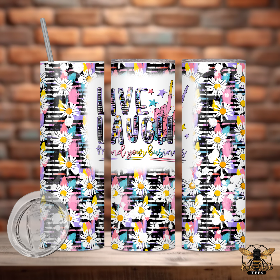 Three colorful tumblers with floral and geometric designs on a wooden surface with a brick wall background.