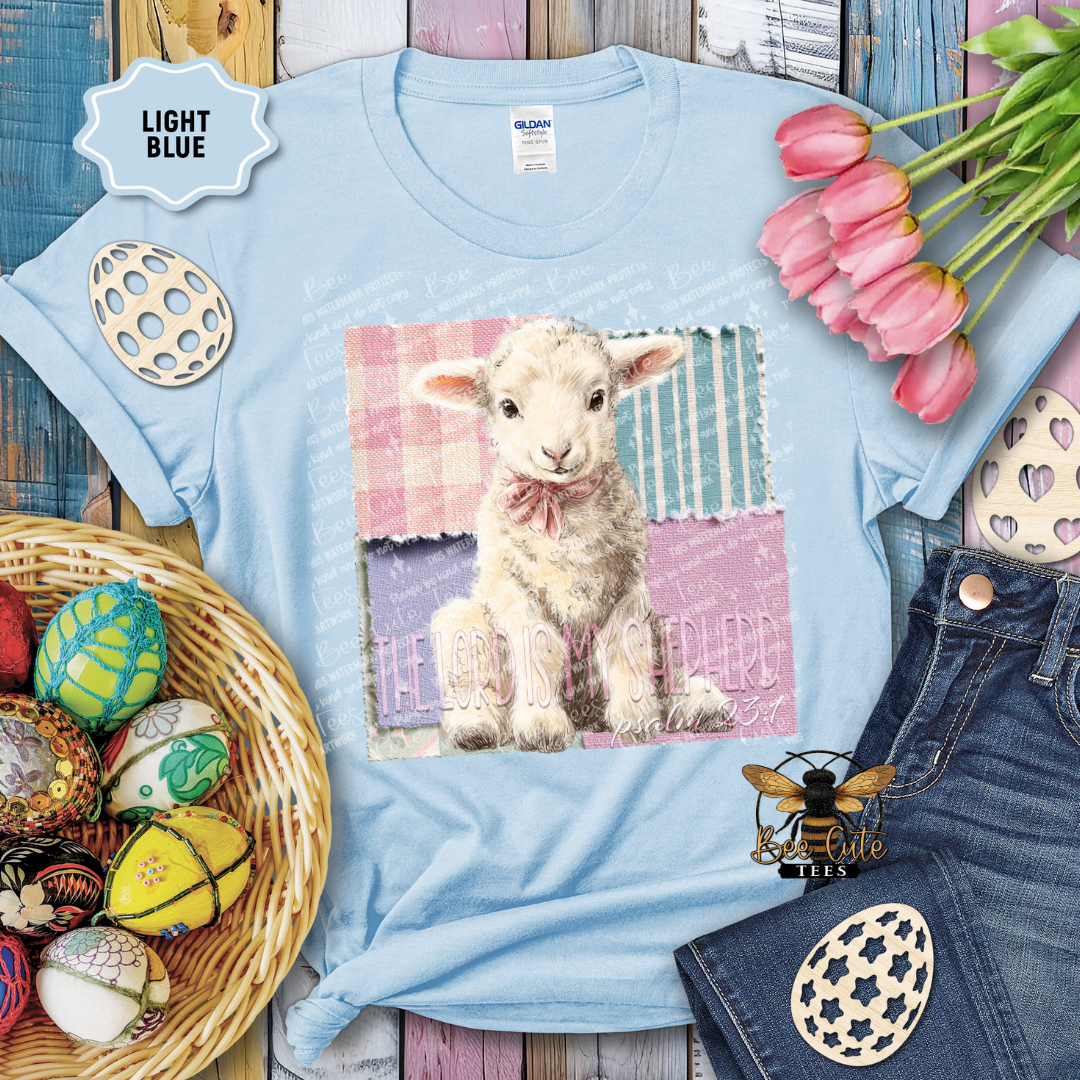 Light blue t-shirt with a lamb graphic and Easter decorations on a wooden surface.