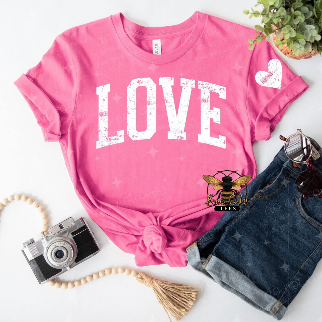 Pink t-shirt with 'LOVE' printed on it, paired with denim shorts and a camera on a white background.