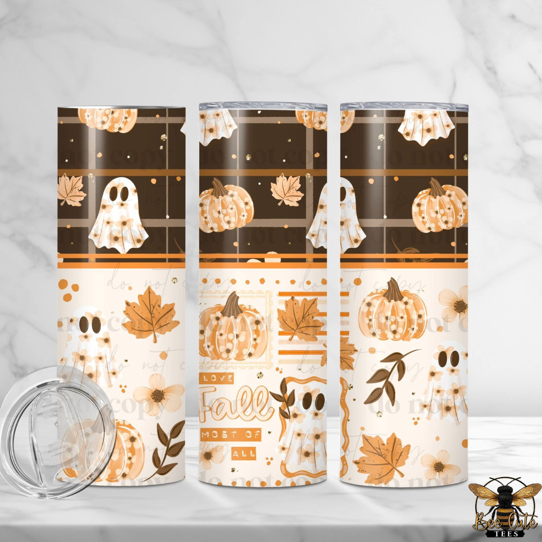 Three tall insulated tumblers with a fall-themed wrap design are displayed on a light marble surface with a marble background. The design features white ghosts, orange pumpkins, and autumn leaves on a cream and dark brown background.