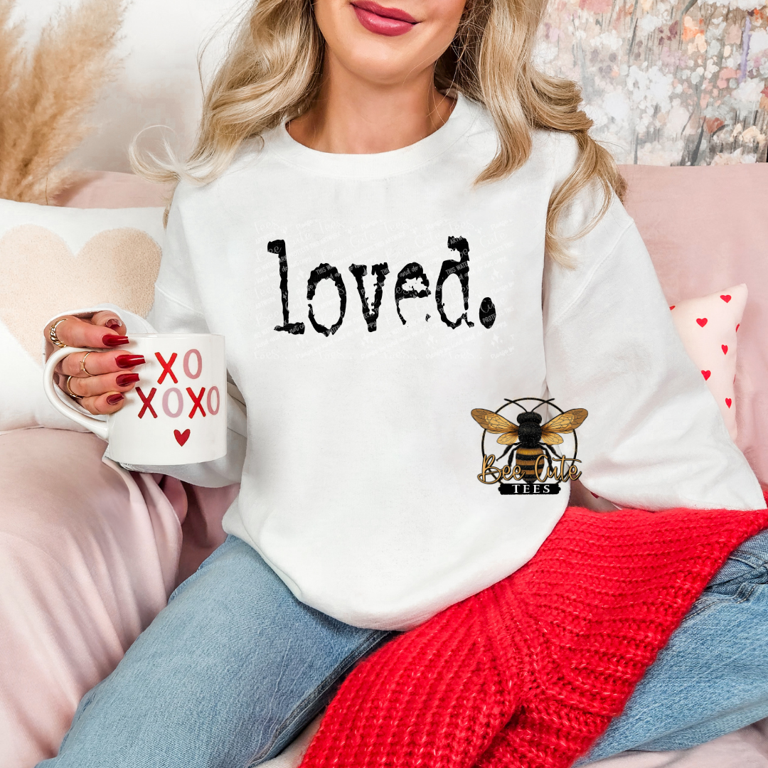 Woman wearing a white sweatshirt with 'loved.' and a bee design, holding a mug with heart designs.
