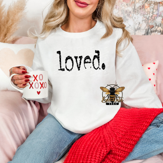 Woman wearing a white sweatshirt with 'loved.' and a bee design, holding a mug with heart designs.
