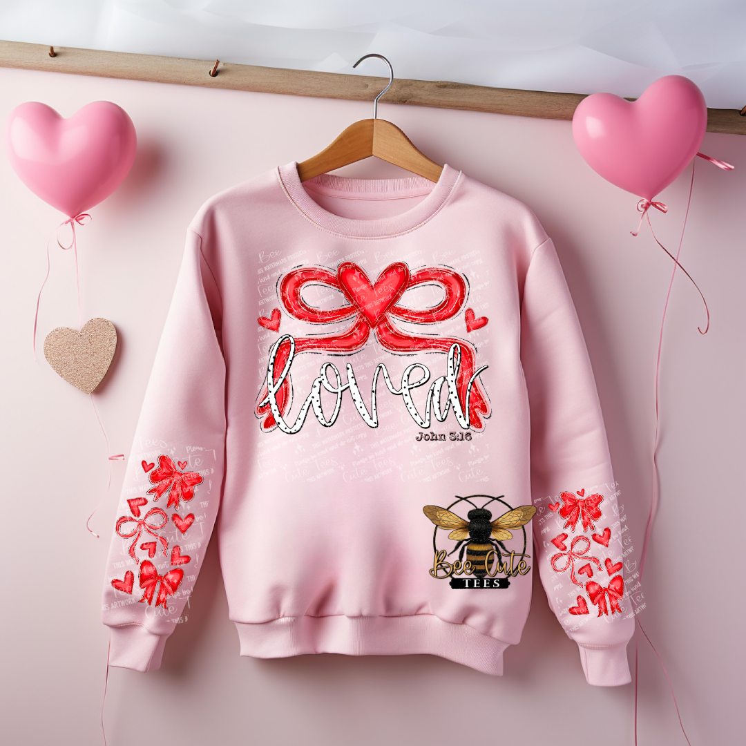 Pink sweatshirt with red heart designs and text, hanging on a wooden rod with pink balloons in the background.