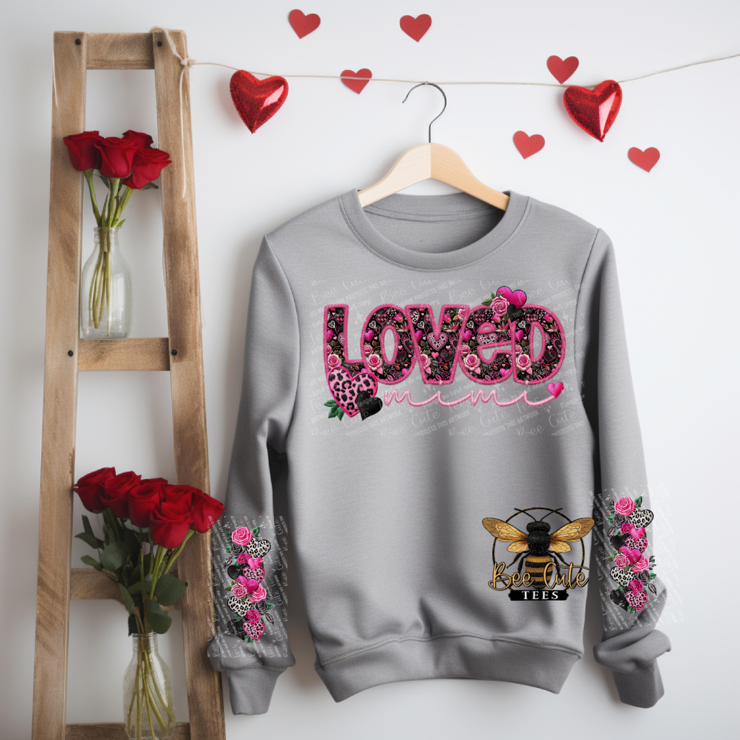 Gray sweatshirt with 'LOVED' design hanging on a wooden hanger with red roses and heart decorations.