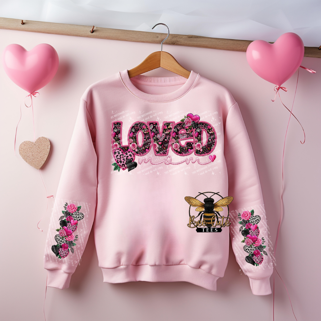 Pink sweatshirt with floral designs and 'LOVED' text on a pink background with heart balloons.