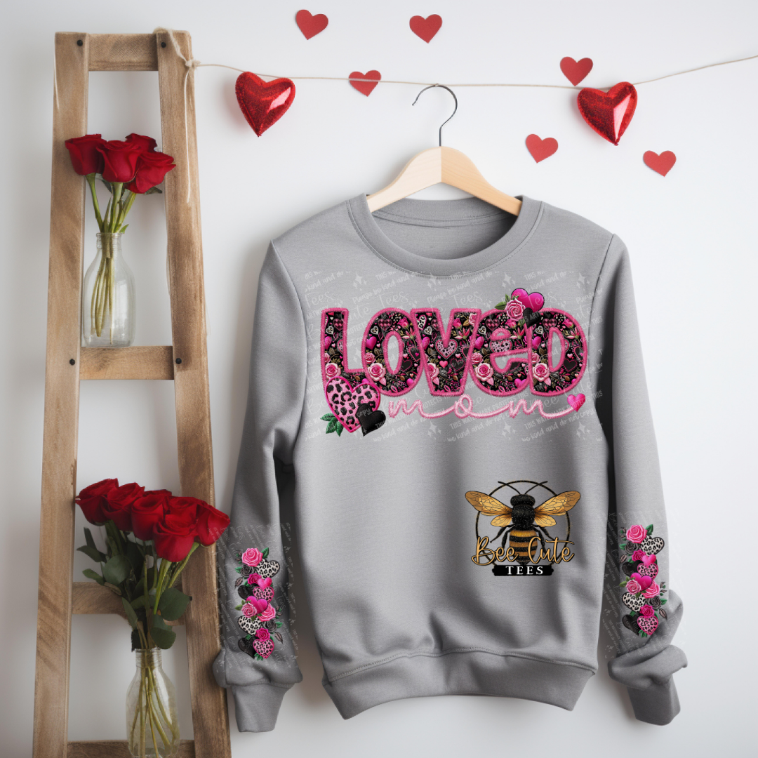 Gray sweatshirt with floral 'LOVED' design hanging on a wooden hanger with red roses and heart decorations.