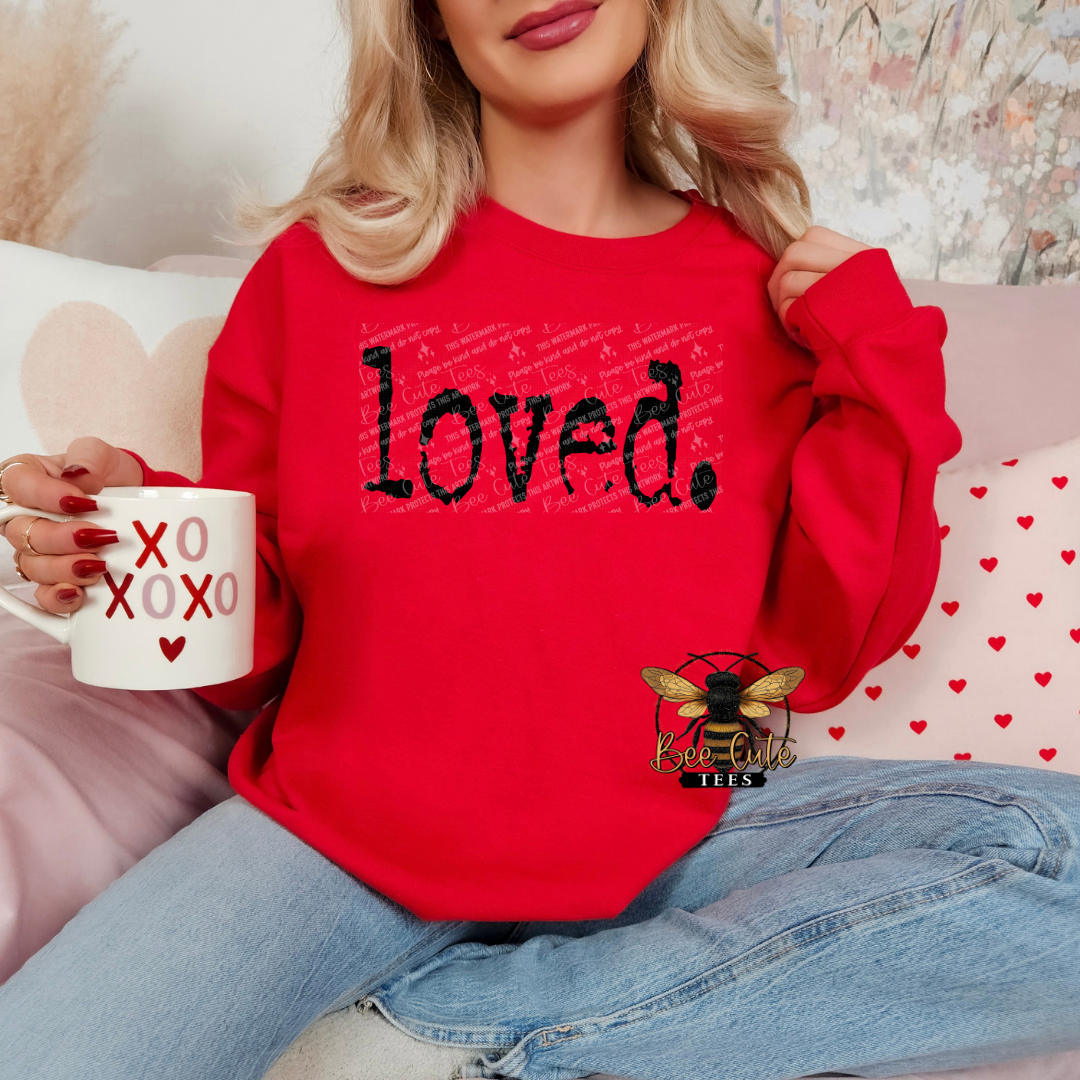 Person wearing a red sweatshirt with 'loved.' text, holding a mug with heart designs, sitting on a couch.