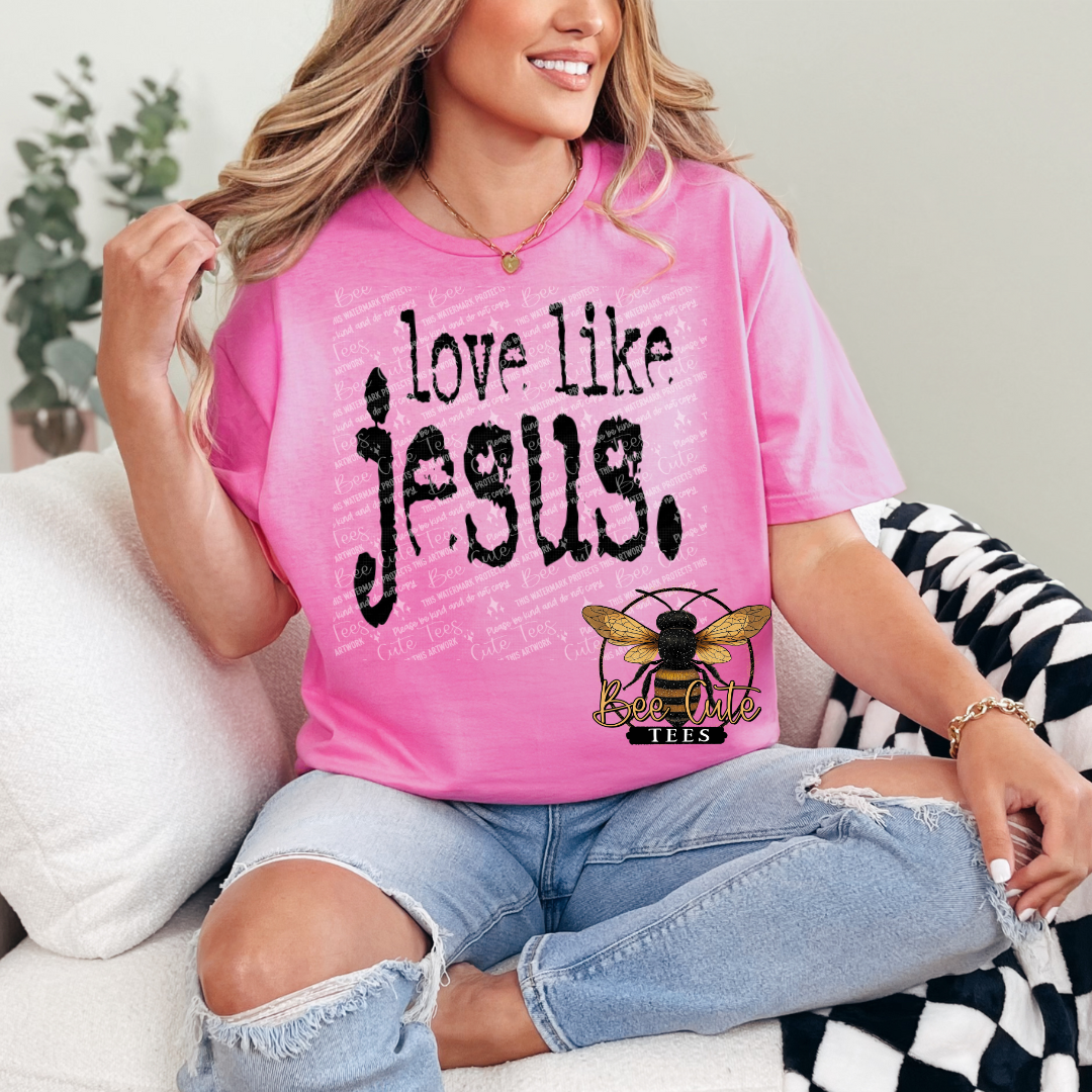 Person wearing a pink t-shirt with 'Love like Jesus' text, sitting on a couch.