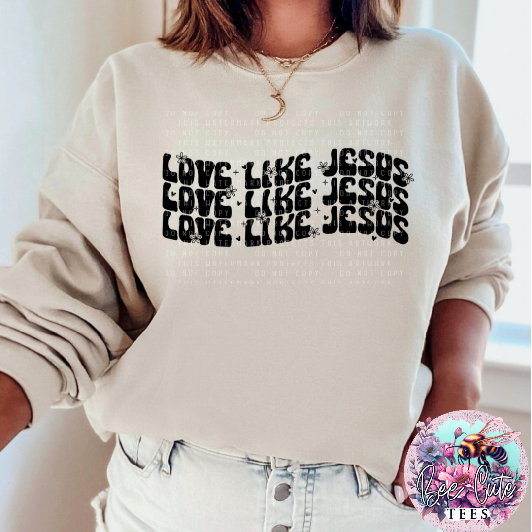 Beige sweatshirt with 'Love Like Jesus' text worn by a person, with a brand logo in the corner.