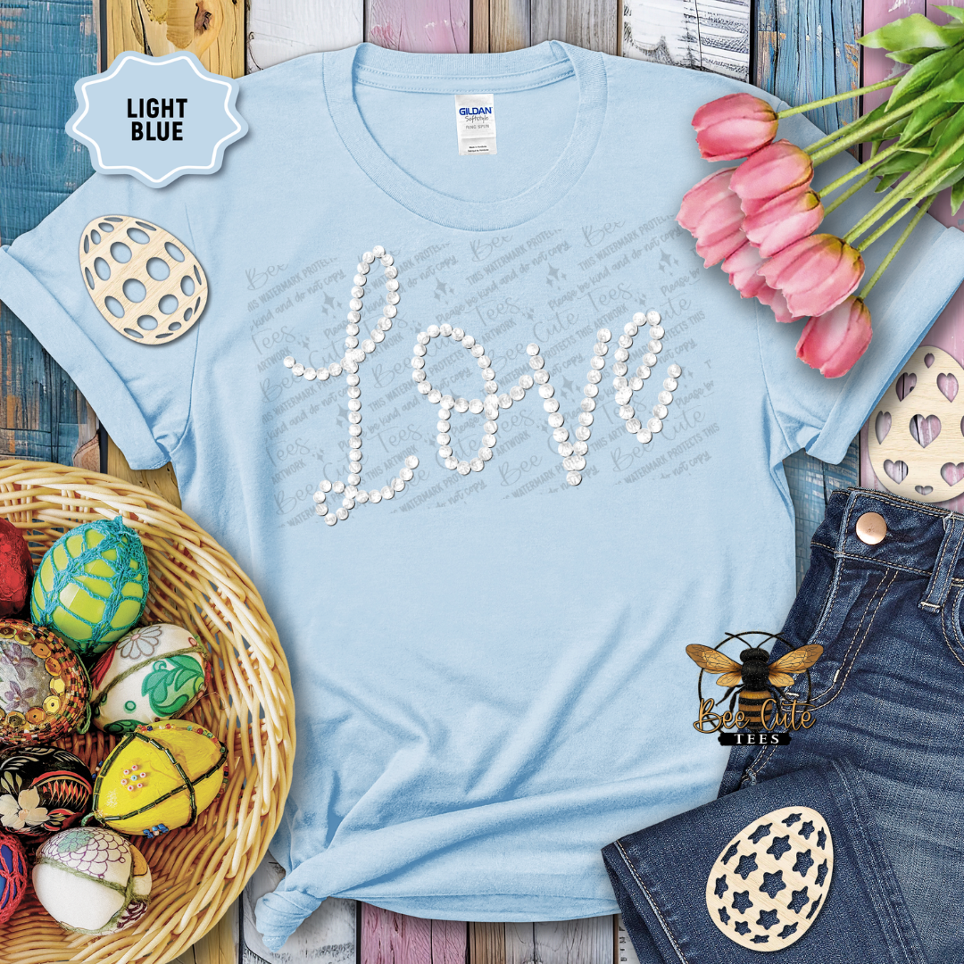 Light blue t-shirt with 'LOVE' design, surrounded by Easter eggs and tulips on a wooden surface.