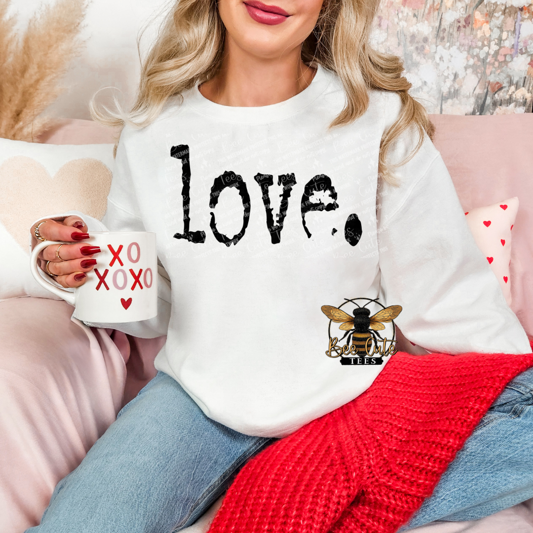 Woman wearing a white sweatshirt with 'Love' and a bee design, holding a mug with heart designs.