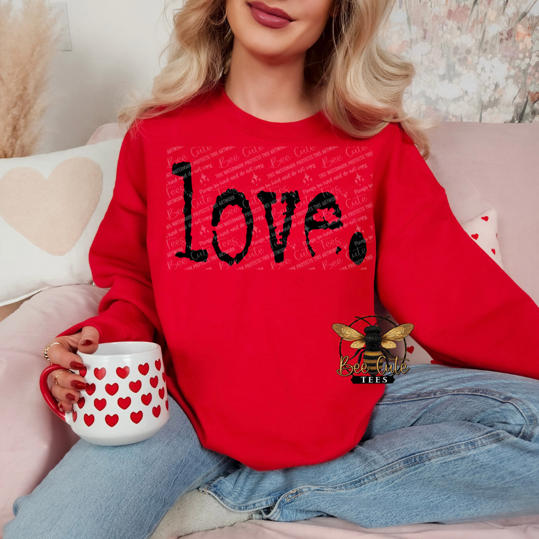 Person wearing a red sweatshirt with 'LOVE.' text, holding a mug with heart pattern, sitting on a couch.