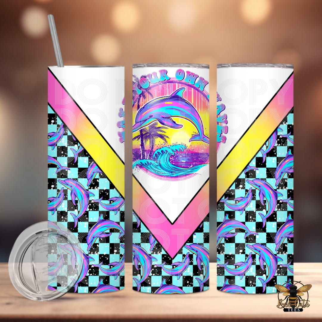 Bright and colorful 20 oz tumbler featuring a vibrant dolphin beach sunset design with “Make Your Own Waves” wording, accented with pastel pink, yellow, and turquoise diagonal details and a checkerboard dolphin pattern wrap, displayed with a lid and metal straw against a softly lit background.

