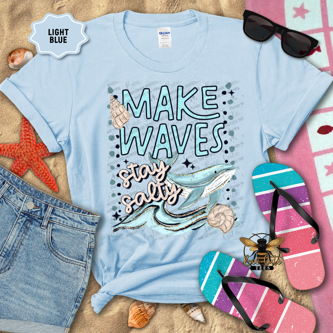 Light Blue t-shirt with 'Make Waves, Stay Salty' design on a beach-themed background with sunglasses, flip-flops, and starfish.