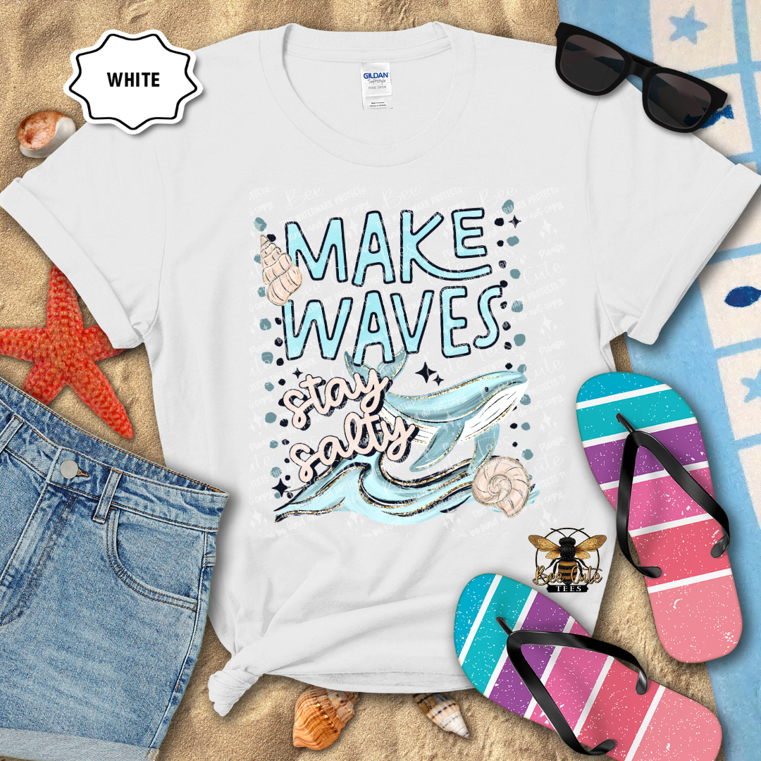 White t-shirt with 'Make Waves Stay Salty' design on a beach-themed background with sunglasses, flip-flops, and denim shorts.