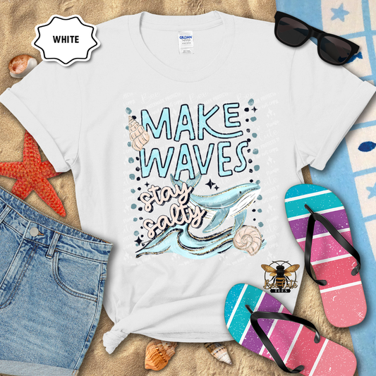 White t-shirt with 'Make Waves Stay Salty' design on a beach-themed background with sunglasses, flip-flops, and denim shorts.