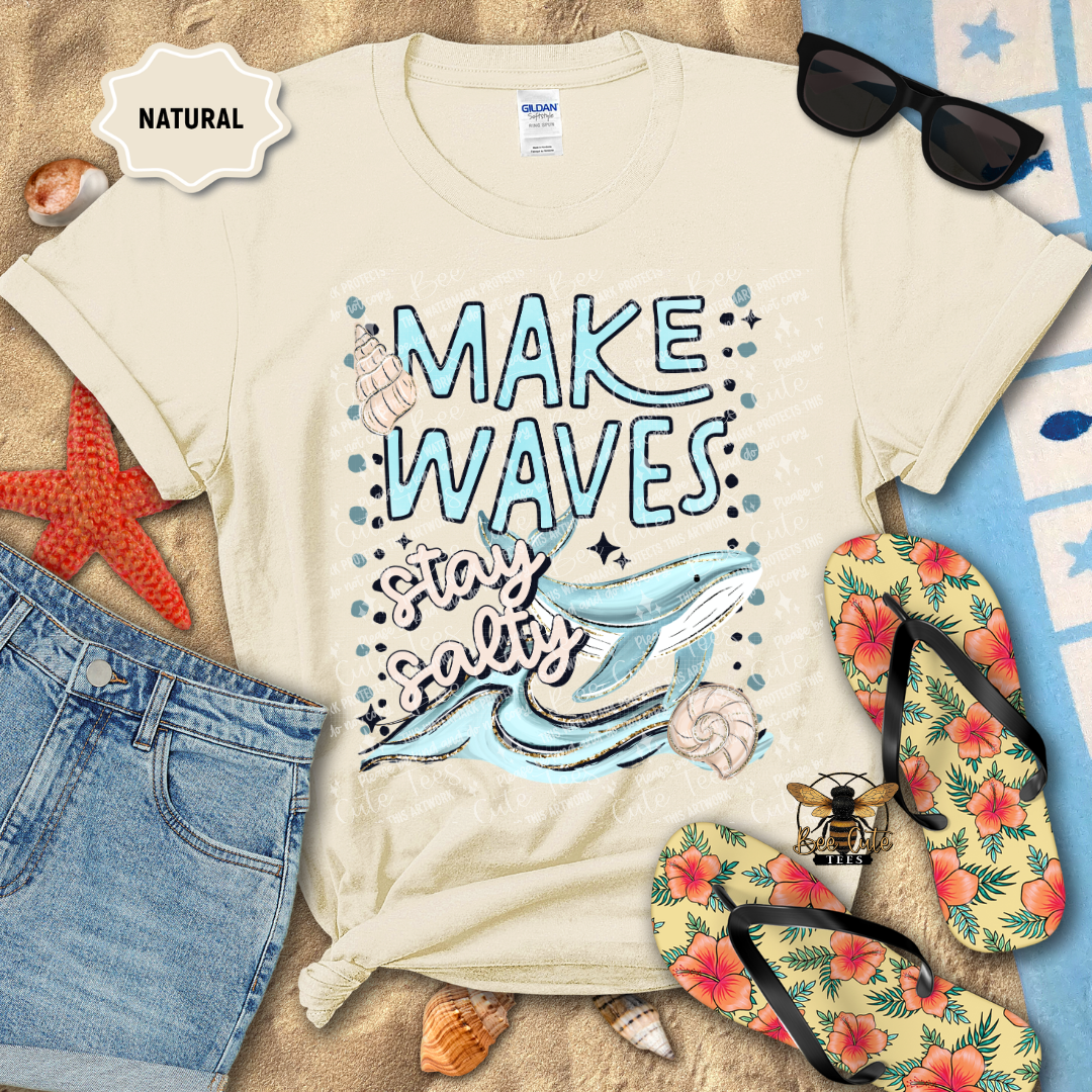 Beige t-shirt with 'Make Waves, Stay Salty' design on a beach-themed background with sunglasses, flip-flops, and starfish.