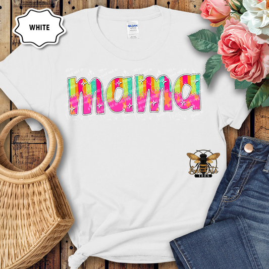 White t-shirt with colorful 'mama' design on a wooden surface with flowers and jeans.