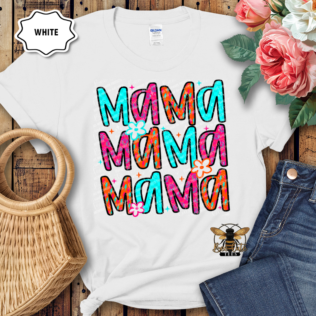 White t-shirt with colorful 'Mama' text design on a wooden surface with flowers and denim jeans.