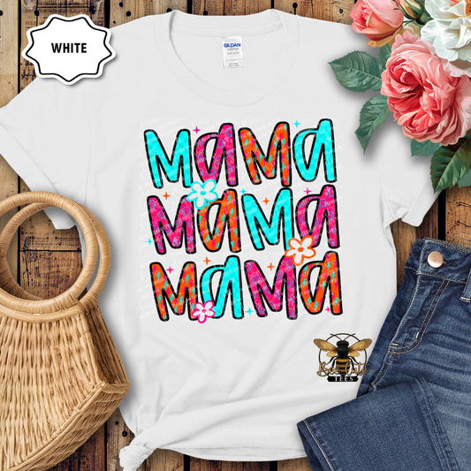 White t-shirt with colorful 'Mama' text design on a wooden surface with flowers and denim jeans.