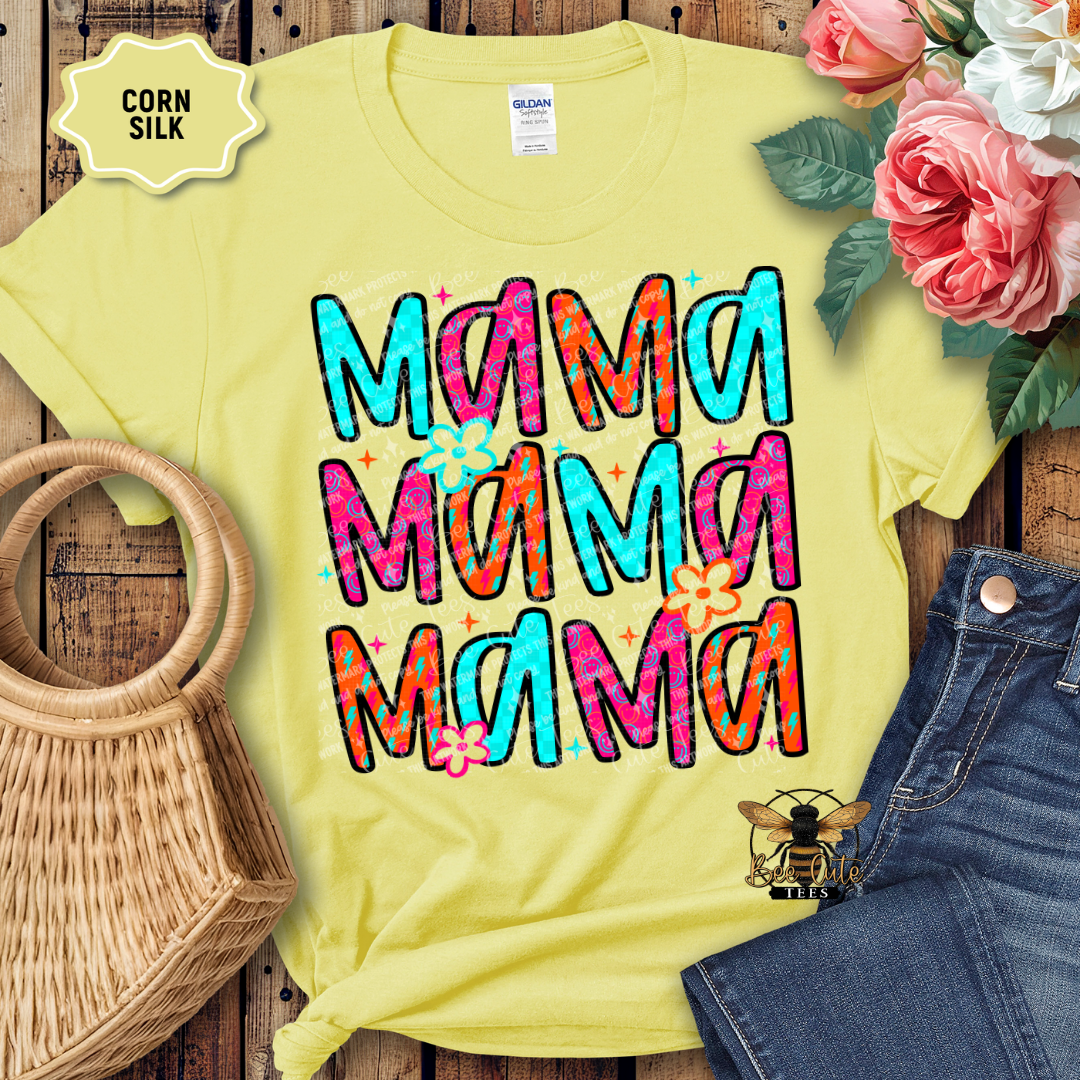 Yellow t-shirt with colorful 'Mama' text, surrounded by flowers, a bag, and jeans on a wooden surface.