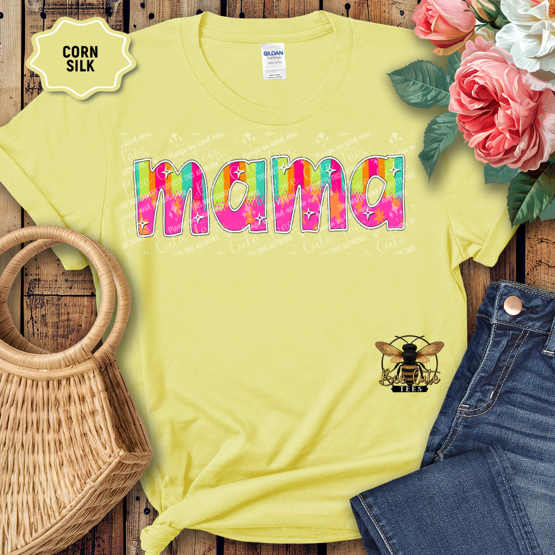 Yellow t-shirt with 'Mama' in colorful letters on a wooden surface with flowers and denim jeans.
