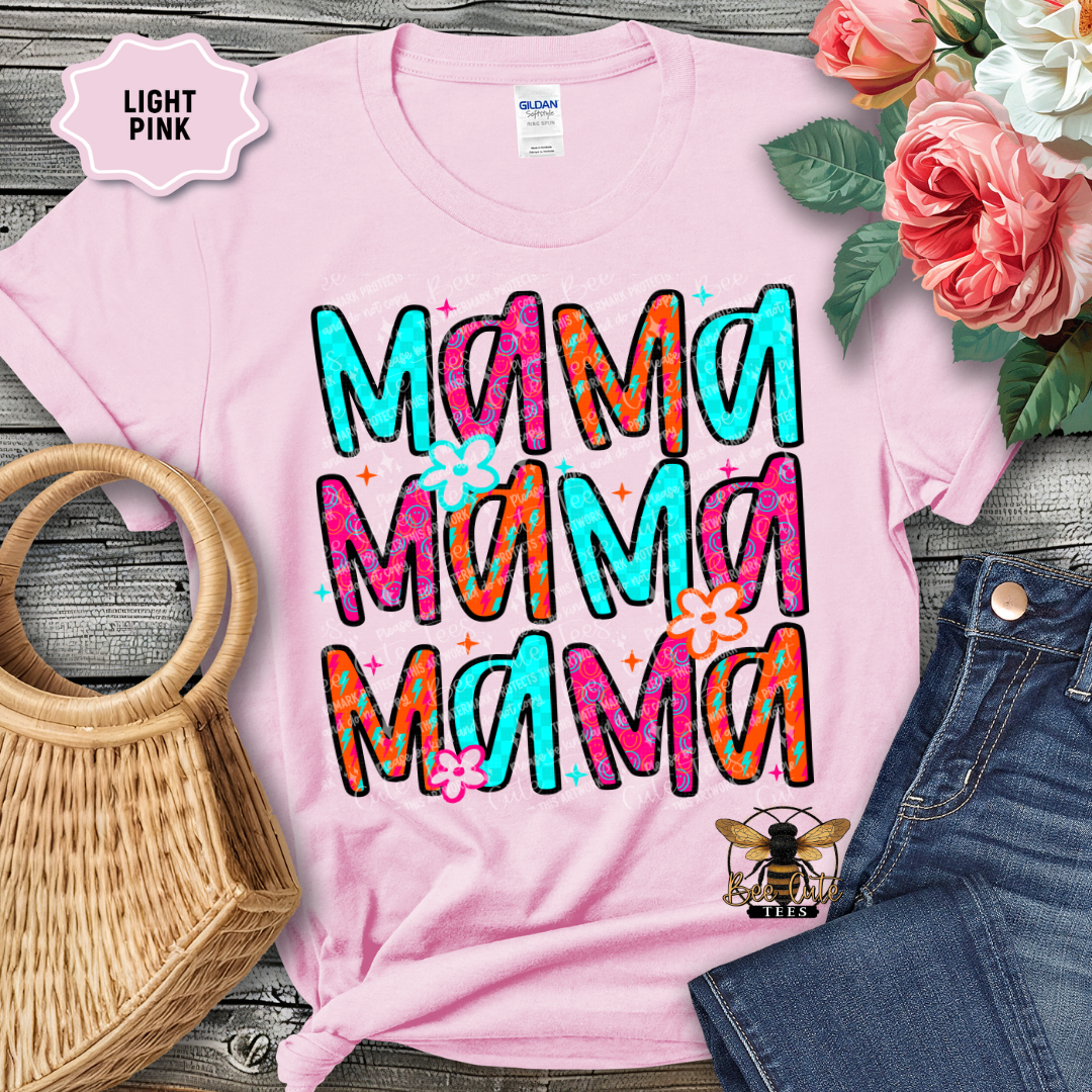 Pink t-shirt with colorful 'Mama' text, placed on a wooden surface with flowers and a handbag.