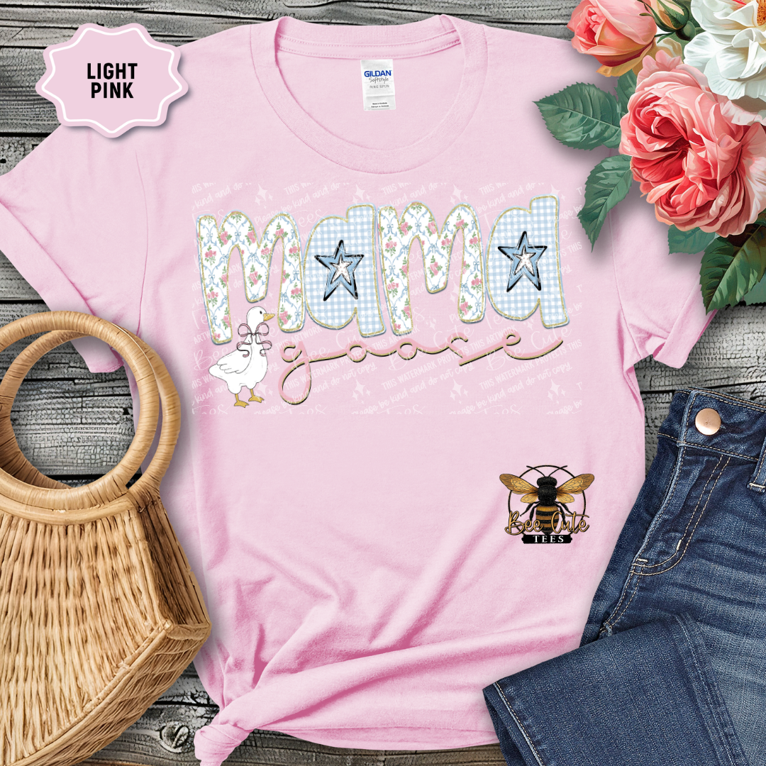 Light pink t-shirt with 'MAMA' design, surrounded by flowers and a handbag on a wooden surface.
